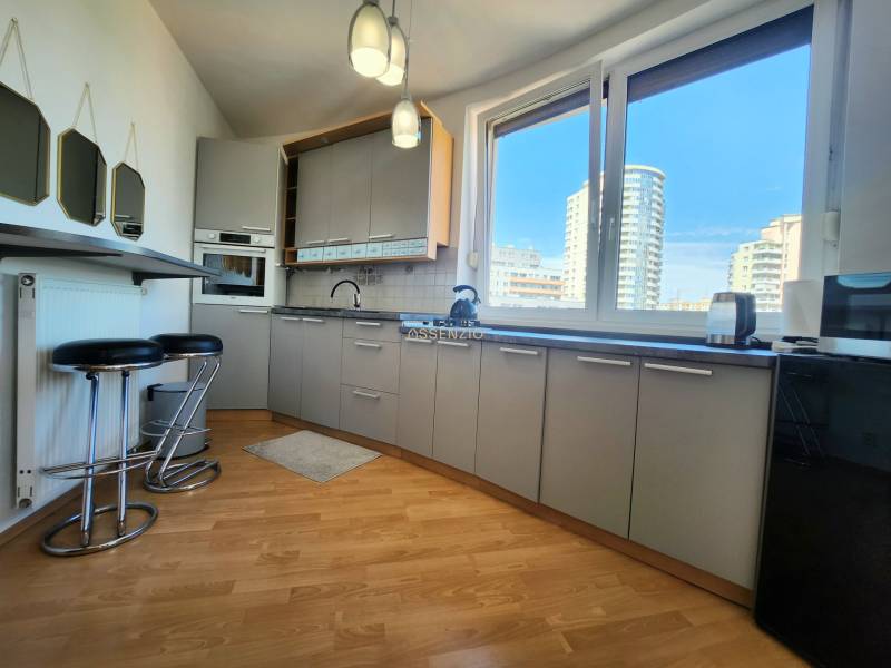 A one-bedroom apartment kitchen with a bar, view of large windows and city skyline.