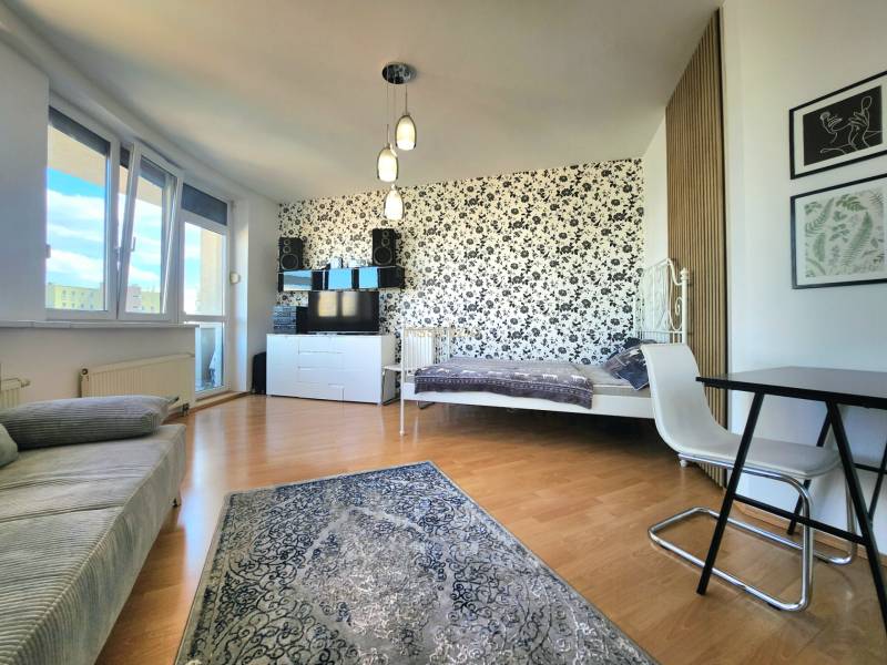 Living room with a bed, floral wallpaper, table, armchair, window with a view.