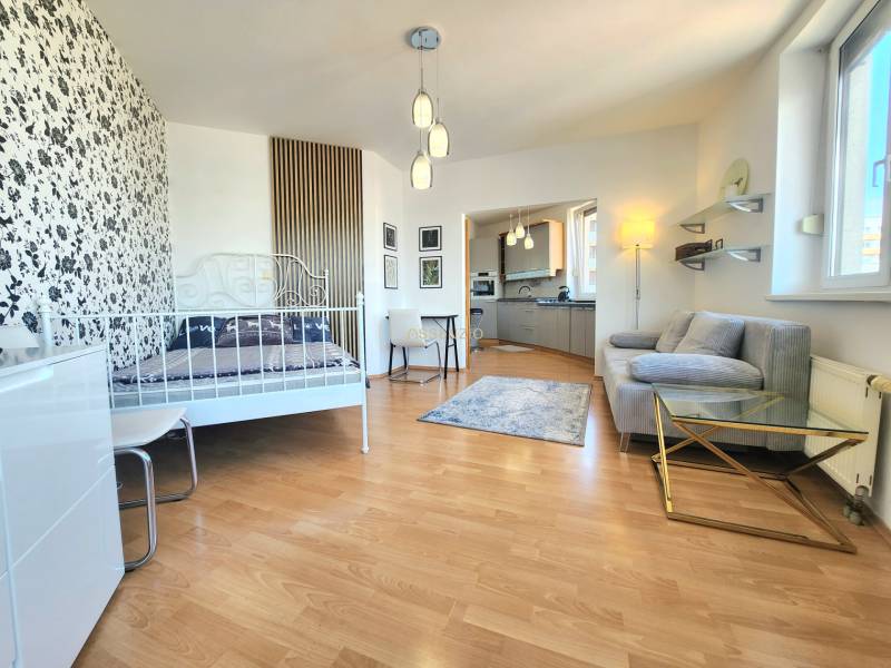 1-bedroom apartment with patterned wallpaper, wooden flooring, kitchen, and seating area.