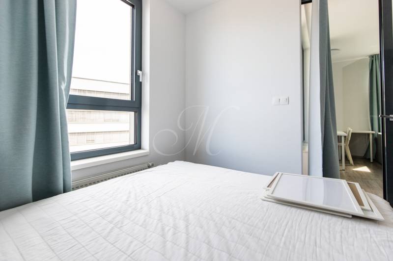 Bright bedroom in a 2-room apartment with curtains and a bed with a white bedspread.