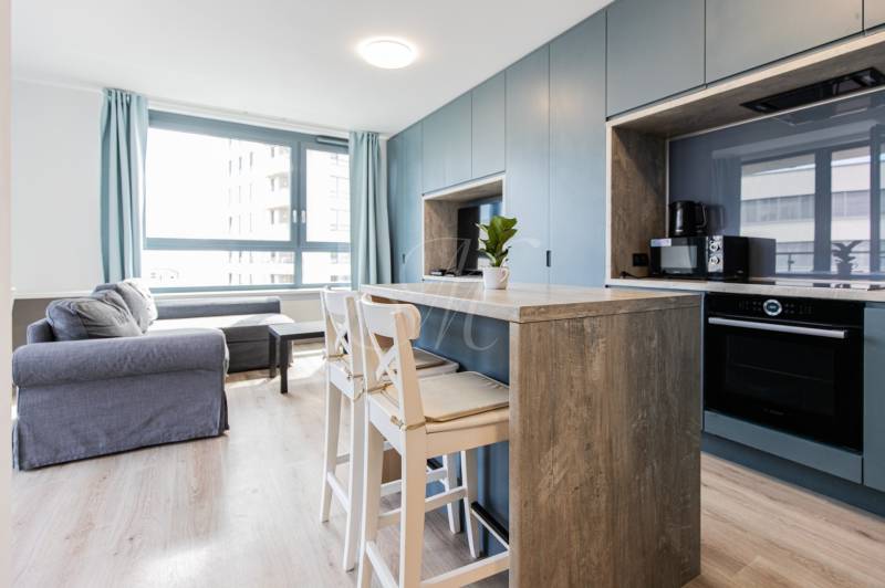 Bright living space with a kitchenette, bar stools, and a large window.