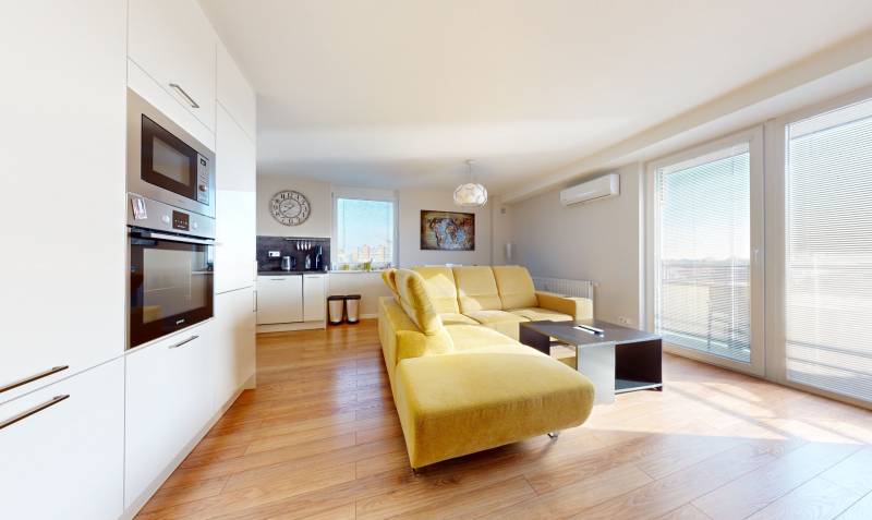 Living room with kitchen in a 3-room apartment with a yellow sofa and white furnishings.