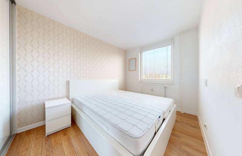 Bright bedroom in a 3-room apartment with a double bed, nightstand, and wooden floor.