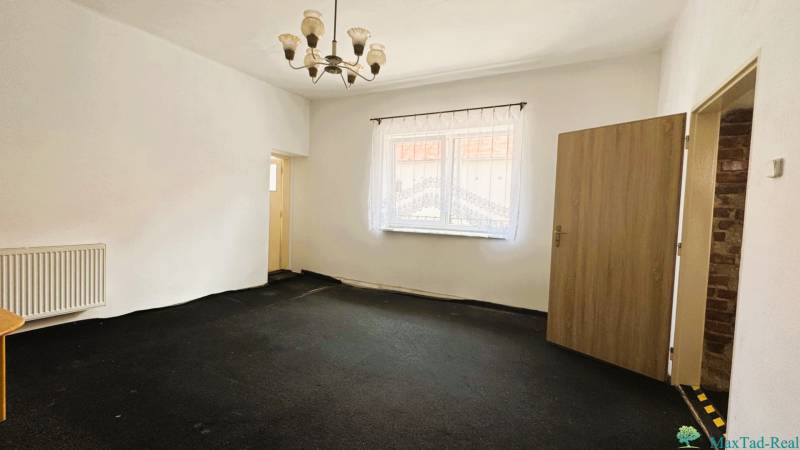 A room in a family house with a curtain on the window, a radiator, and a chandelier.