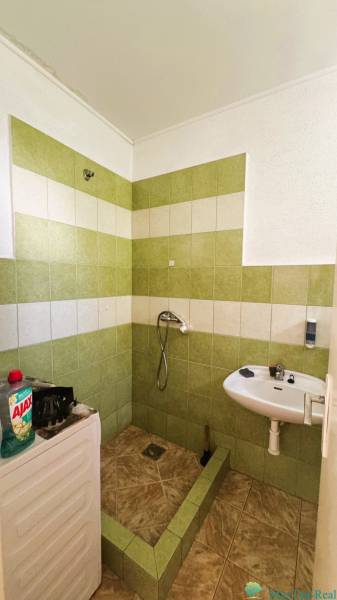 A bathroom in a family house with tiles, a shower, and a sink, next to cleaning products.