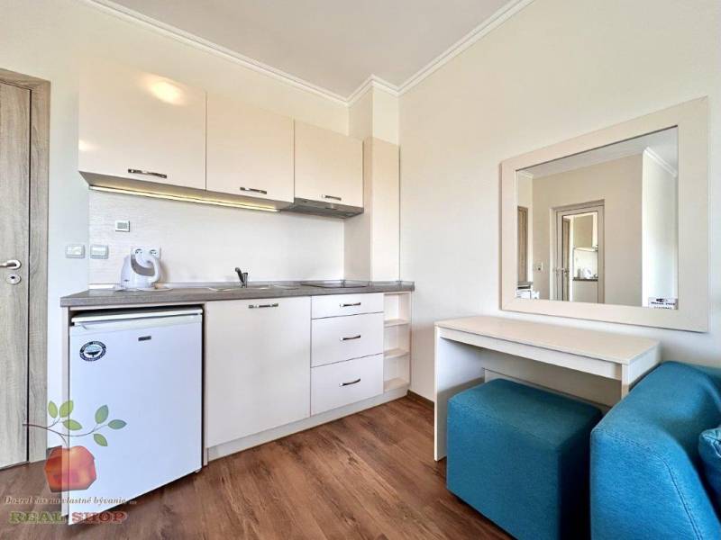 A kitchen area in a holiday apartment with light furniture and a mirror.