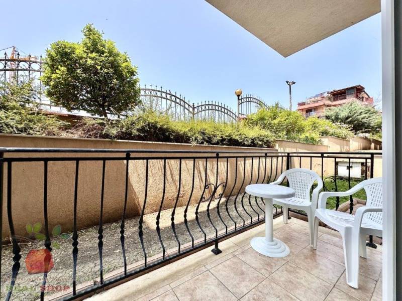 Terrace of a recreational apartment in Nessebar with garden furniture and a view of greenery and a fence.