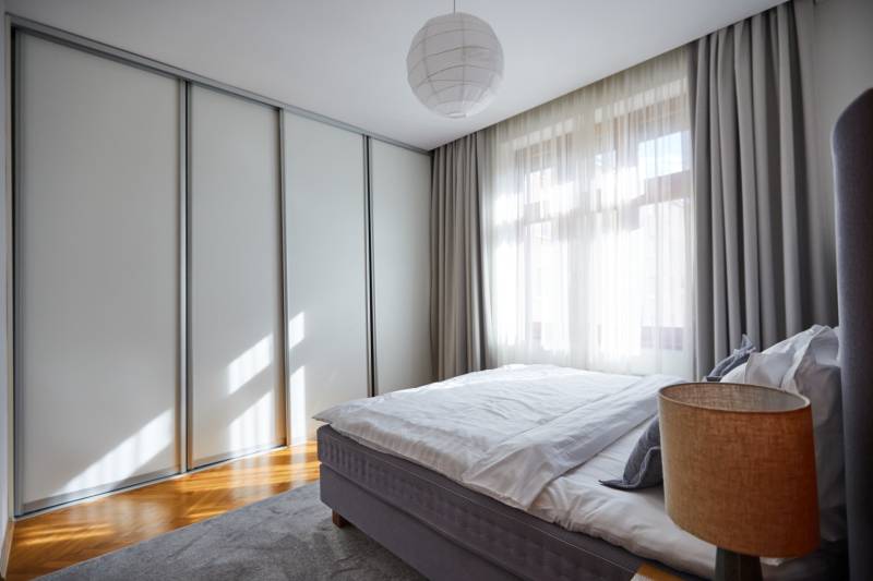Bedroom in a 4-room apartment, bed with a lamp, built-in wardrobe, curtains, daylight.