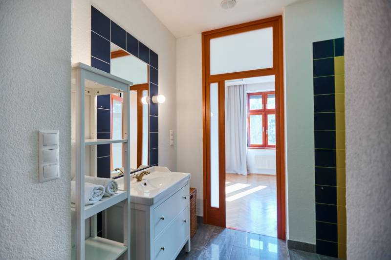 Bathroom entrance with a sink, drawers, mirror, and a view of the sunny room in a 4-room apartment.