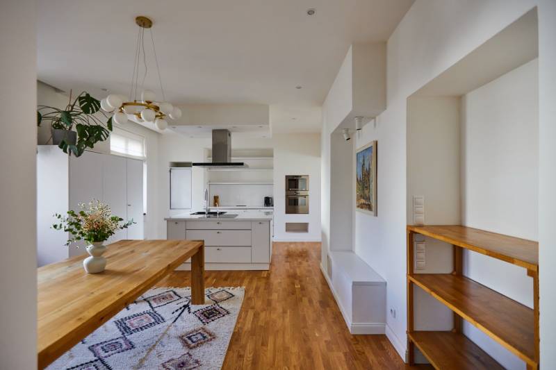A kitchen in a 4-room apartment with a wooden table, floor, and white cabinets.