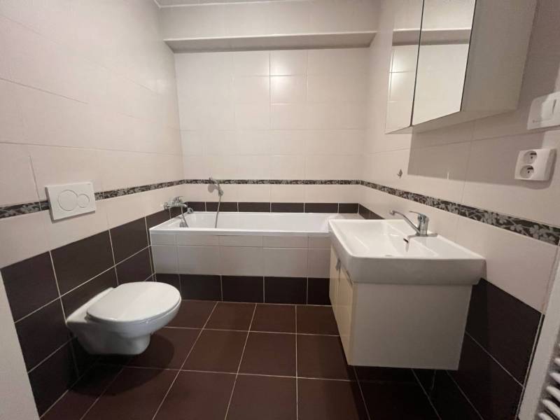 Bathroom in a 3-room apartment with brown and white tiles, a bathtub, a sink, and a toilet.
