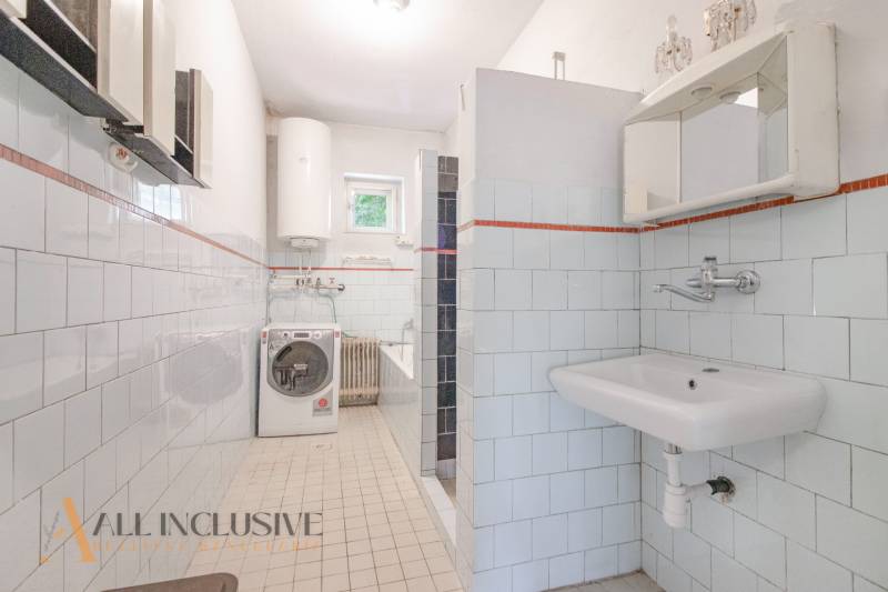 A bathroom in a family house with a shower, sink, washing machine, and boiler.