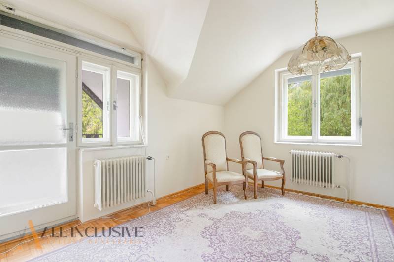A room in a family house with two chairs, a carpet, two windows, radiators.