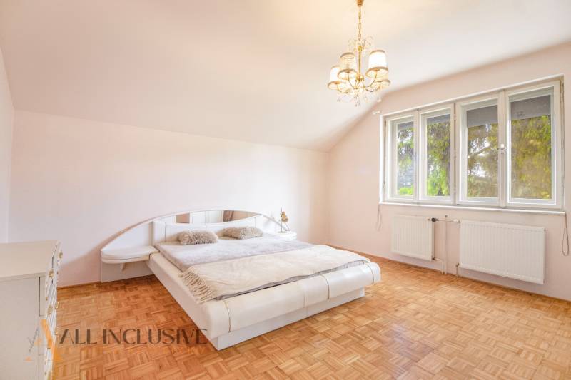 Bright bedroom with a large bed, wooden floor, and chandelier in a family house.