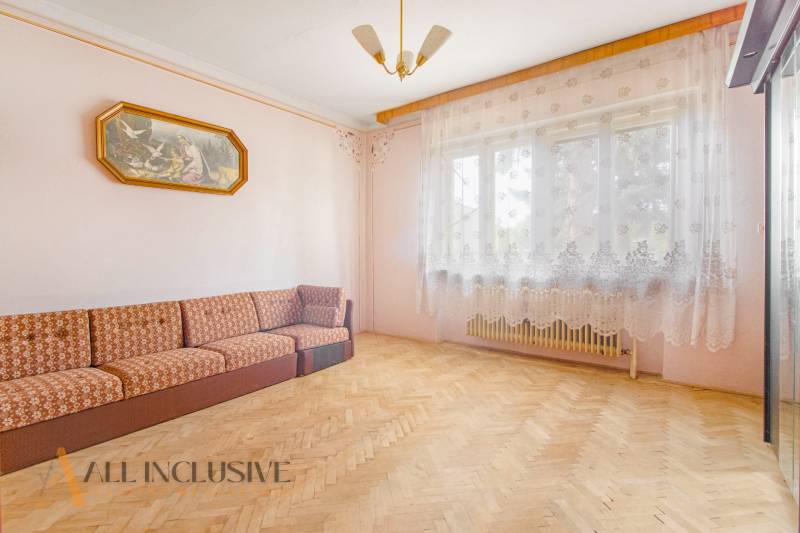 A bright room with a sofa in a family house, sheer curtains, and wooden flooring.