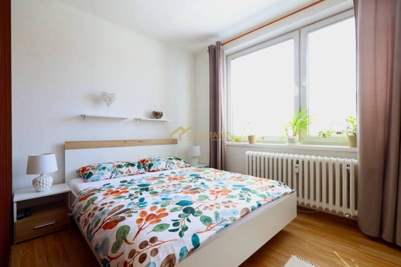 A bright bedroom with a patterned bed and plants in a two-room apartment.