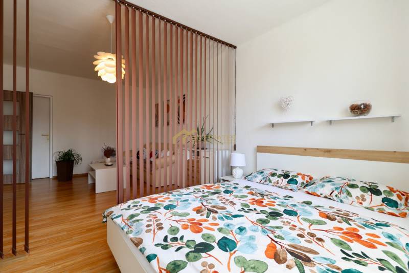 Bedroom in a 2-room apartment with patterned bed linen and wooden flooring.
