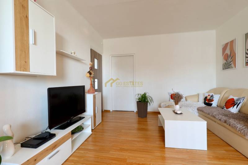 Living room in a two-room apartment with wooden flooring, white furniture, and decorations.
