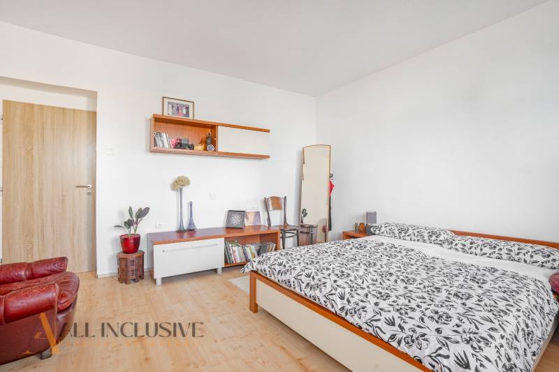 Bedroom in a family house with a double bed, shelves, and an armchair, light-colored walls.