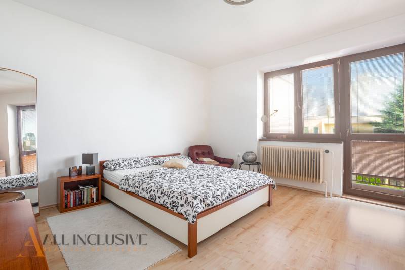 A bright bedroom with a large window, a bed, and a chair in a family house.