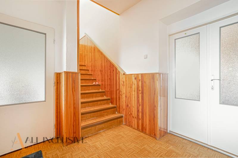 The family house has a hallway with a staircase and wooden paneling.