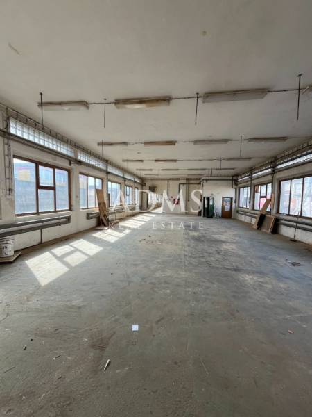 An empty warehouse interior with windows, gray flooring, and hanging lights.