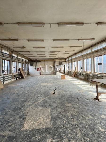 An abandoned room with a damaged floor in an industrial hall, light penetrating through the windows.