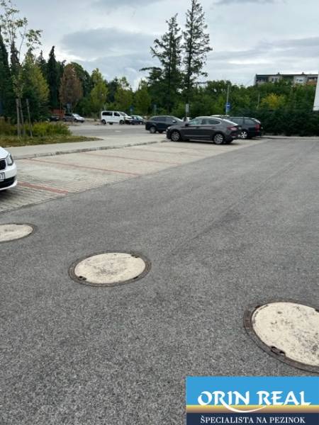 Parking lot on Za dráhou Street in Pezinok with cars and trees in the background.