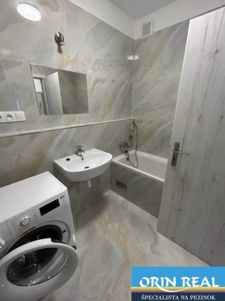 Bathroom with a shower and a washing machine in a 2-room apartment with white walls and a mirror.