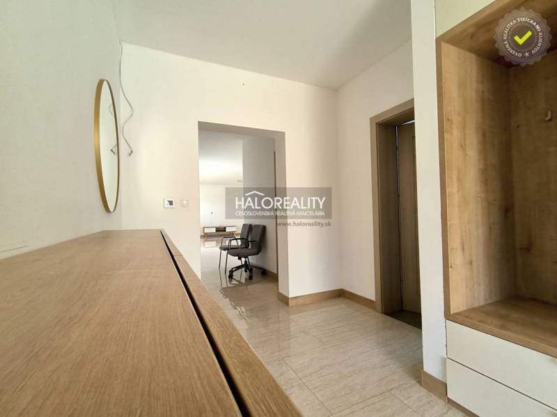 A hallway in a family house with wooden furniture, a mirror, and tiles leads to the living area.