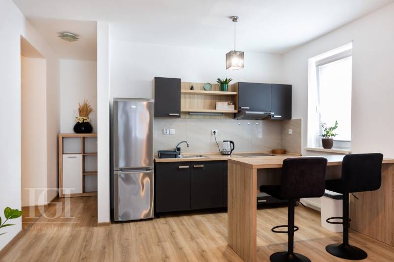 A kitchen in a 2-room apartment with a wooden floor, a bar counter, and a refrigerator.