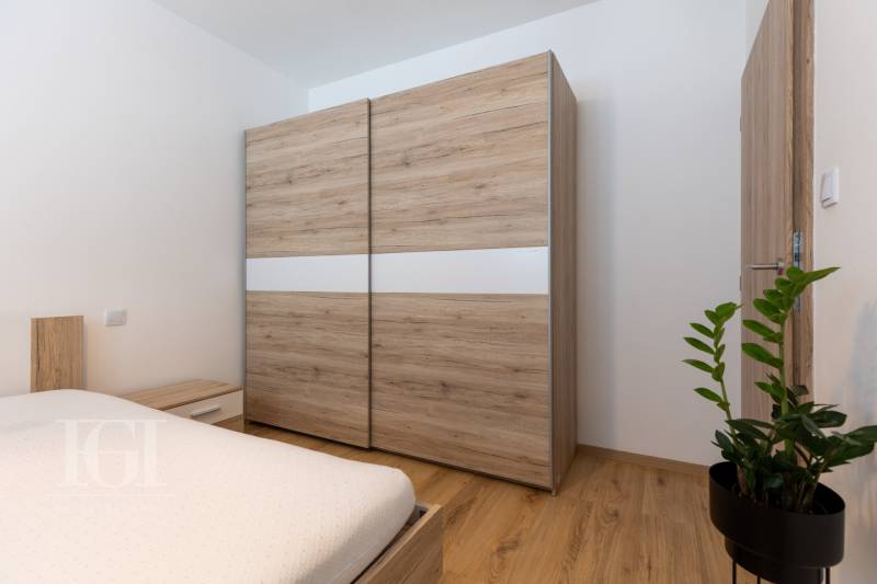A bedroom with a wooden wardrobe and bed in a 2-room apartment, complemented by a green plant.