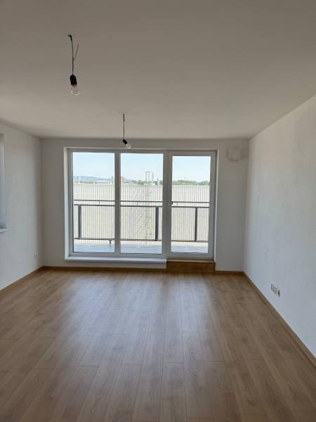 A spacious room with wooden flooring and large windows in a 2-room apartment.