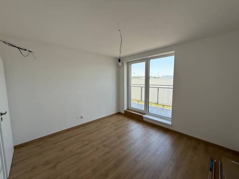 A room in a 2-bedroom apartment with a wooden floor and a large window to the balcony.