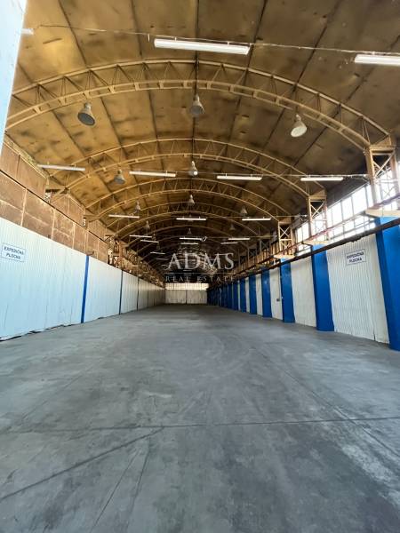Interior of warehouses and halls with high ceilings, steel beams, and a row of lights.
