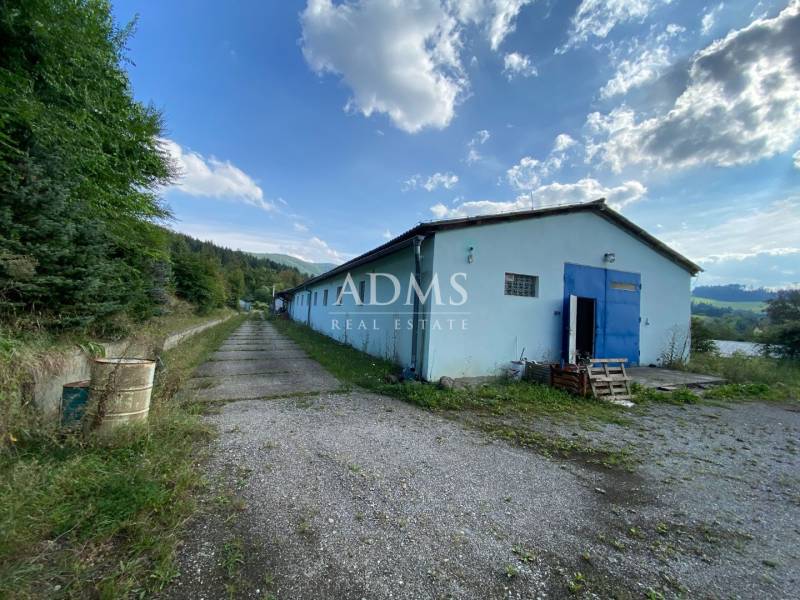 Warehouses and halls in Považská Bystrica, surrounded by greenery and a blue sky.