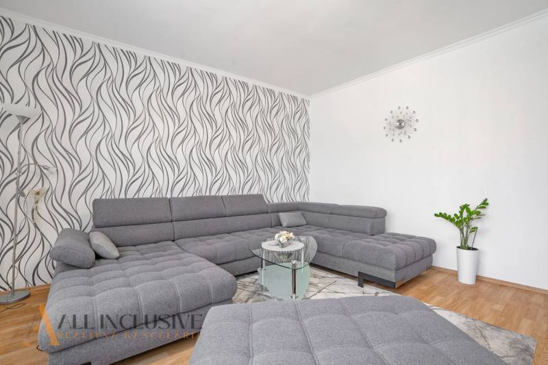 A bright living room in a two-room apartment with a gray sofa and patterned wallpaper.
