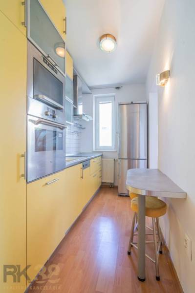 A kitchen in a 3-room apartment with wooden flooring, modern appliances, and a bar counter.