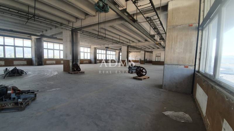 A spacious hall with machines, large windows, and concrete columns.