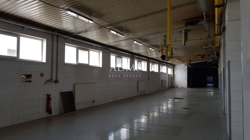 A spacious interior with white walls, piping, windows, and a fire extinguisher in warehouses and halls.