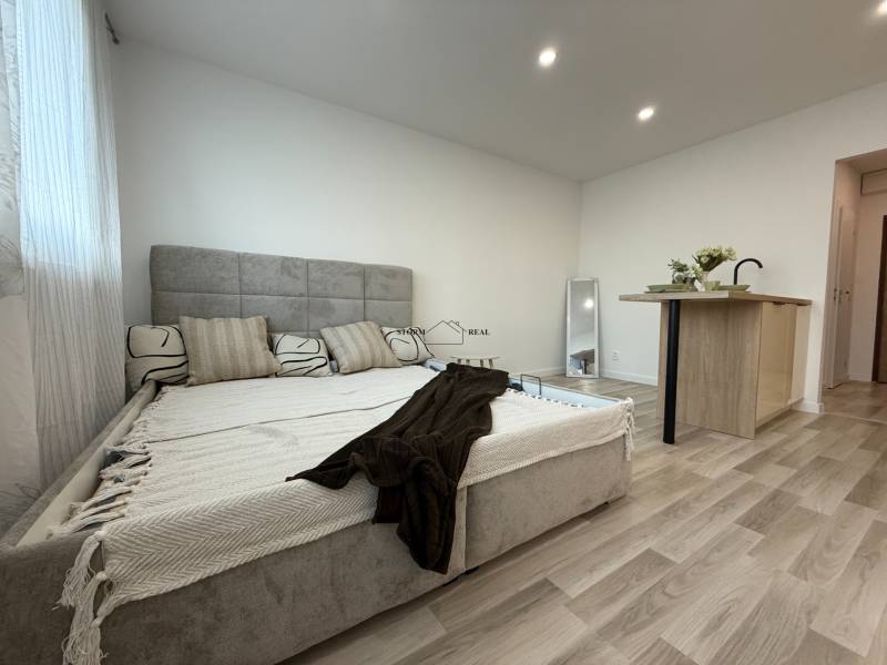 A studio apartment with a bed, kitchen island, and decorative pillows in an open space.