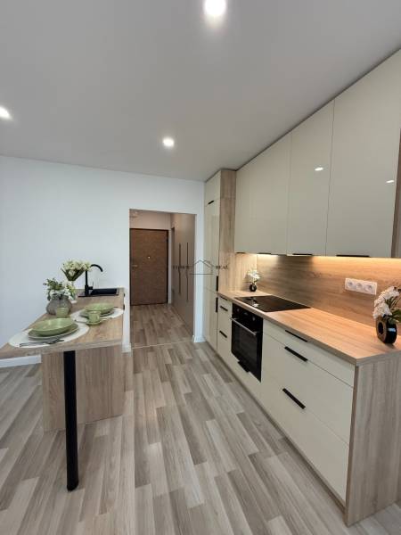 A kitchen in a studio apartment with wooden flooring, white cabinets, and a dining table.