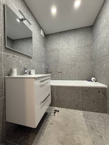 Bathroom with a bathtub and a sink in a studio apartment, with tiles and a mirror.