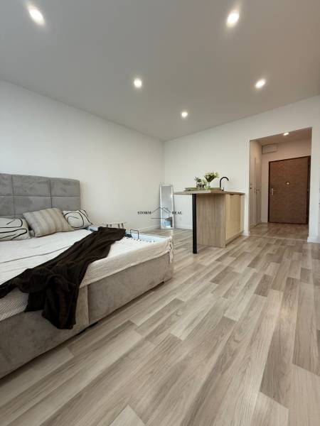 A bed with a wooden floor and a kitchen counter in a studio apartment.