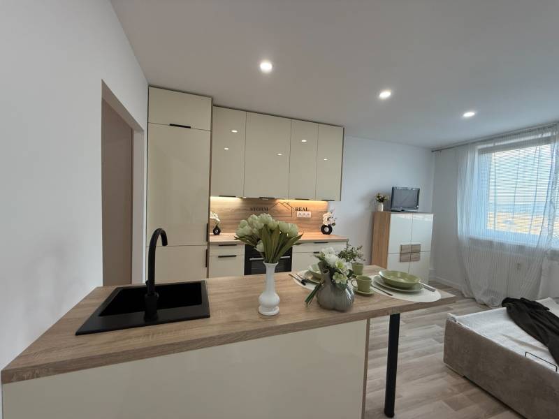 Kitchen of a one-room apartment with a dining counter and a sofa, illuminated by lights.