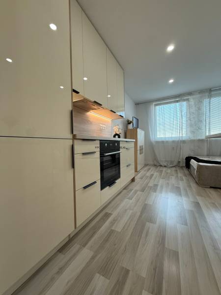 A kitchen in a studio apartment with wooden flooring and built-in appliances.