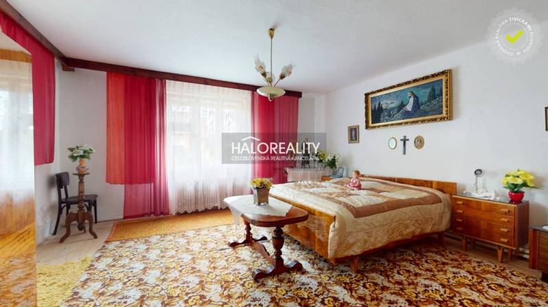 A bedroom in a family house with red curtains, a double bed, and decorative paintings.