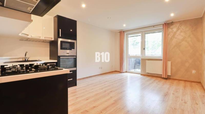 A kitchen in a 3-room apartment with a light wooden floor design and built-in appliances.