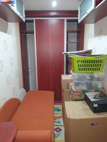 A narrow space with an orange couch, cabinets, and stored boxes in a 2-room apartment.