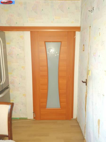 Wooden sliding doors in the entrance of a 2-room apartment with patterned wallpaper.